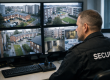 Security officer monitoring CCTV screens showing a council housing estate in a public sector control room.