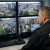 Security officer monitoring CCTV screens showing a council housing estate in a public sector control room.